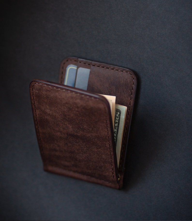 May include: A brown leather wallet with a money clip and a credit card slot. The wallet is closed and has a bill sticking out of the top.