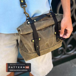 May include: An olive green waxed canvas messenger bag featuring black leather straps with gold-tone metal rivets and a matching shoulder strap attachment. The bag has a roll-top design and a rectangular label reading MUSAK PATTERNS PATTERN FOR MACHINE SEWING.