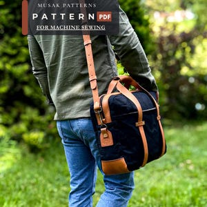Könnte beinhalten: Eine schwarze Umhängetasche aus Segeltuch mit Riemen, Griffen und Bodenverstärkungen aus hellbraunem Leder. Die Tasche hat einen langen, verstellbaren Schultergurt und Metallbeschläge. Text: MUSAK PATTERNS PATTERN PDF FOR MACHINE SEWING.