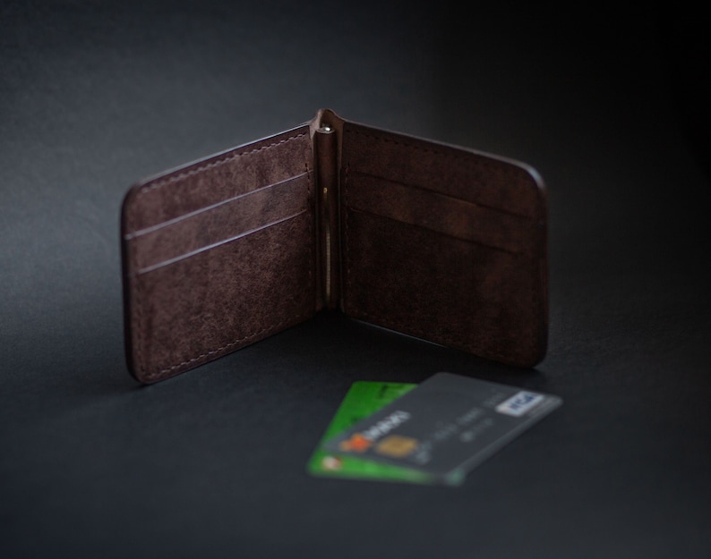May include: A brown leather wallet with a money clip and multiple card slots. The wallet is open and there are two credit cards visible.