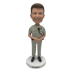 Op de afbeelding: Een bobblehead-beeldje van een glimlachende officier in een lichtgroen uniform met een badge en radio. Het beeldje staat op een witte basis met de tekst "CHP Officer". Het uniform van de officier heeft donkerblauwe strepen.