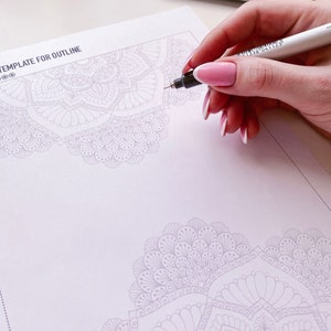 Puede incluir: Una mano sostiene un bol&iacute;grafo blanco y negro y delinea un dise&ntilde;o de mandala detallado en una hoja de papel blanca. El papel tiene el texto "TEMPLATE FOR OUTLINE" en la parte superior.