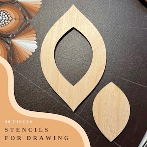 Op de afbeelding: Twee houten sjablonen om te tekenen, een grote en een kleine, beide in de vorm van een blad. De tekst "28 PIECES STENCILS FOR DRAWING" is zichtbaar in de afbeelding.