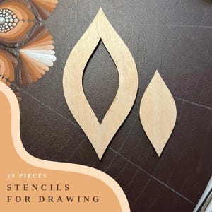 Op de afbeelding: Twee houten stencils in de vorm van een blad, een groter dan de andere. De stencils liggen op een bruin oppervlak. De tekst "28 PIECES STENCILS FOR DRAWING" is zichtbaar in de linkerbenedenhoek van de afbeelding.