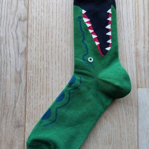 May include: Green and black socks with a crocodile graphic. The crocodile's mouth is open and has white teeth and a red tongue.