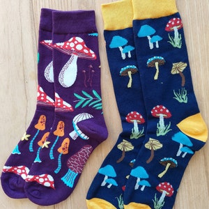 Peut inclure: Deux paires de chaussettes colorées avec des motifs de champignons. Une paire est violette avec des champignons rouges et blancs, l'autre est bleu marine avec des champignons rouges, blancs et bleus.