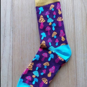 May include: A pair of purple socks with a colourful mushroom pattern. The socks have a yellow cuff and a turquoise toe and heel.