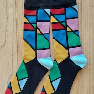 May include: A pair of black socks with a colorful geometric pattern. The pattern features squares and triangles in shades of red, blue, yellow, green, and pink.