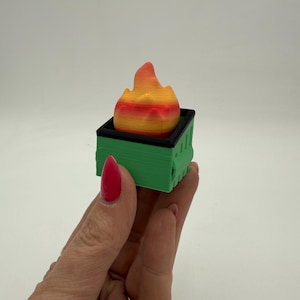 May include: A small green trash can with a black rim and a bright orange and yellow flame on top.