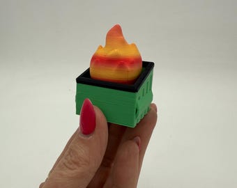 May include: A small green trash can with a black rim and a bright orange and yellow flame on top.
