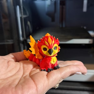 Op de afbeelding: Een klein, 3D-geprint drakenbeeldje met rode en gele schubben. De draak heeft een stekelige kam en vleugels.