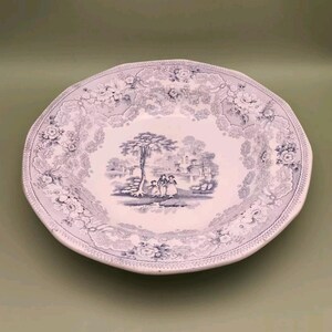 Könnte beinhalten: Eine weiße Suppenschüssel aus Keramik mit einem blauen und weißen Blumenmuster. Die Schüssel zeigt eine zentrale Szene mit einem Baum und einer Brücke mit drei Figuren im Vordergrund.