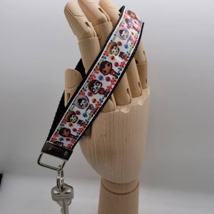 Puede incluir: Un llavero blanco y negro con una cinta colorida con personajes de dibujos animados. La cinta tiene un fondo blanco con flores coloridas y personajes de dibujos animados. El llavero tiene un llavero de plata y una llave de plata.