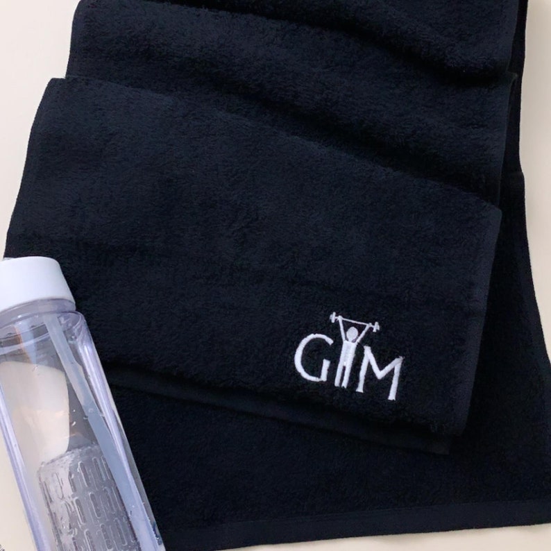K&ouml;nnte beinhalten: Schwarzes Sporttuch mit wei&szlig; gesticktem Text "GIM" und einer Strichm&auml;nnchenfigur, die Gewichte hebt.