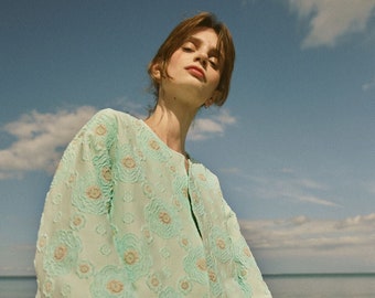 An impressive bomber-style kimono with a beautiful jacquard weave and the shape of an inflatable bomber jacket in the color of sea water on a Greek beach