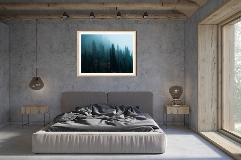 May include: A framed landscape art print of a misty forest scene hangs above a bed with gray bedding. The room has a modern design with concrete walls, wooden accents, and a large window.