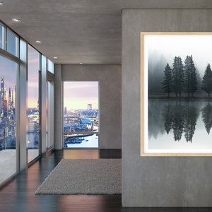 May include: A framed photograph of a misty forest scene with five tall trees reflected in a still body of water. The trees are dark green and the water is a light gray. The photograph is hanging on a gray wall in a modern interior.