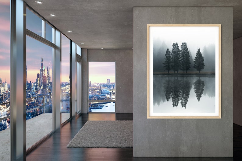 May include: A framed photograph of a misty forest scene with five tall trees reflected in a still body of water. The trees are dark green and the water is a light gray. The photograph is hanging on a gray wall in a modern interior.