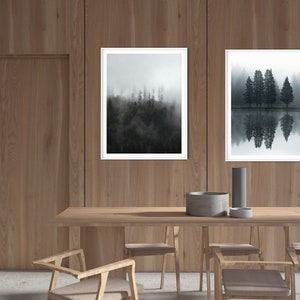 May include: Two framed black and white photographs of trees and reflections in water hanging on a wood wall above a wooden table with chairs.