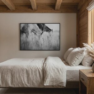 Pu&ograve; includere: Una camera da letto con una tavolozza di colori neutri. Un letto con piumino e cuscini beige &egrave; al centro. Una stampa incorniciata in bianco e nero di cavalli al pascolo nell'erba alta &egrave; appesa sopra il letto. Un comodino in legno contiene un vaso di pampas.