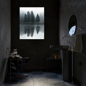 May include: A black bathroom vanity with a round sink and a black pedestal. The vanity is in front of a window with a view of a foggy forest. There are toiletries on a small table next to the vanity.