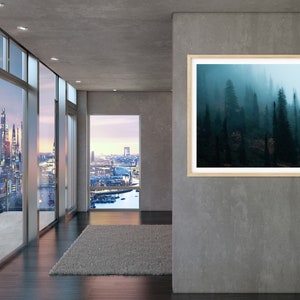 May include: A framed landscape art print featuring a misty forest scene. The artwork is displayed in a modern interior with large windows offering city views. The print has a light wood frame and a serene, natural theme.