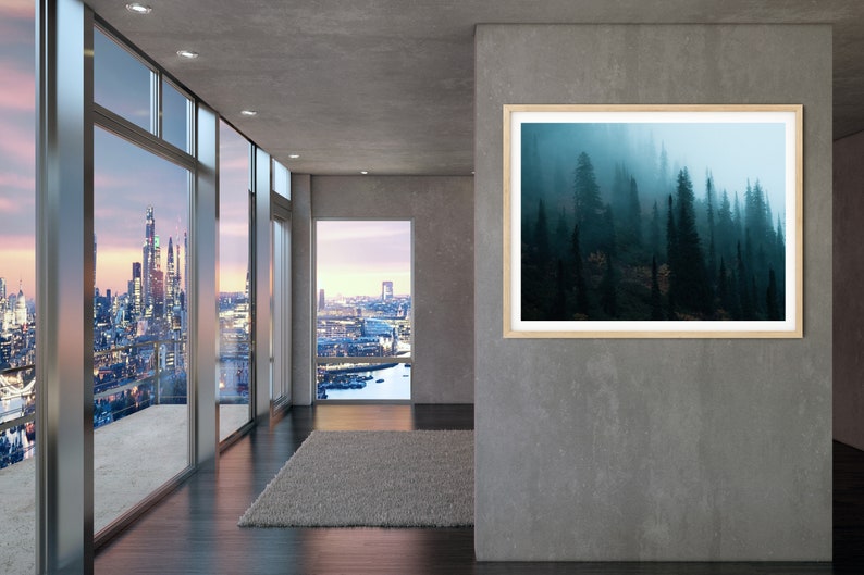 May include: A framed landscape art print featuring a misty forest scene. The artwork is displayed in a modern interior with large windows offering city views. The print has a light wood frame and a serene, natural theme.