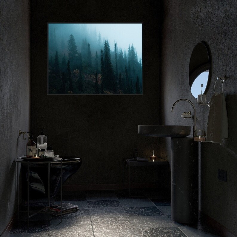 May include: A dark, moody bathroom with a framed landscape of a misty forest. The room features a black sink, toilet, and a small side table. A round mirror and towel rack are also visible.