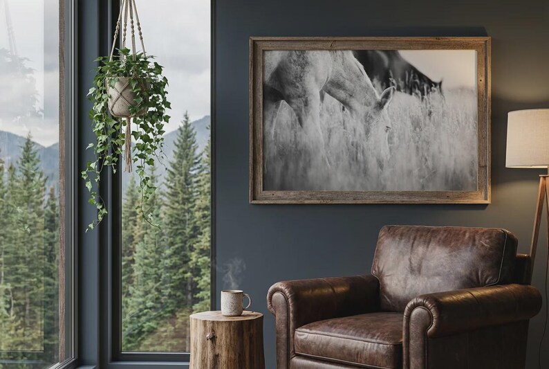 Pu&ograve; includere: Un'accogliente scena di soggiorno con una fotografia in bianco e nero incorniciata di cavalli in un campo. Una poltrona in pelle marrone &egrave; accanto a un tavolino in legno con una tazza. Una pianta sospesa e una lampada da terra completano l'arredamento.