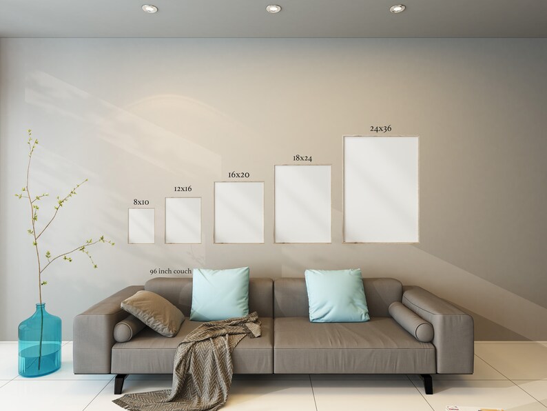Op de afbeelding: Een moderne woonkamer met een grijze bank, lichtblauwe kussens en een patroon plaid. Boven de bank worden vijf ingelijste kunstdrukken van verschillende formaten getoond. Links staat een blauwe glazen vaas met een plant.