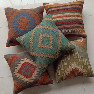 Peut inclure: Quatre coussins décoratifs avec des motifs géométriques dans des tons de brun, vert, bleu et rouge. Les coussins sont en tissu tissé et ont un style rustique et bohème.