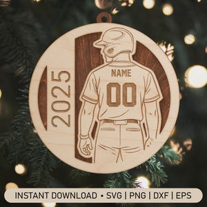 Puede incluir: Adorno de béisbol de madera con un diseño de jugador de béisbol. La camiseta del jugador tiene el número "00" y un espacio para un nombre. El año "2025" está grabado en el lateral. El adorno tiene un fondo marrón oscuro.