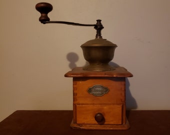 May include: A vintage wooden coffee grinder with a brass top and a drawer. The grinder has a crank handle and a label that reads "Original", "Dresden", and "Germany".