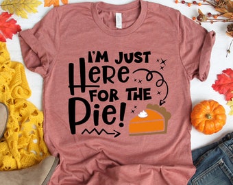 May include: A maroon t-shirt with the text "I'm Just Here For The Pie!" in black. The shirt has a graphic of a slice of pumpkin pie with a swirl of whipped cream on top.