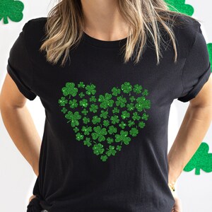 May include: A black t-shirt featuring a green glitter shamrock heart design. The shamrocks are arranged in the shape of a heart.