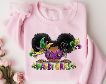 May include: Pink sweatshirt with a cartoon illustration of a Black girl with purple Mardi Gras mask and the text "Mardi Gras".