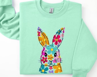 May include: A light green sweatshirt with a floral bunny design. The bunny is made up of colorful flowers in shades of pink, yellow, blue, and green.