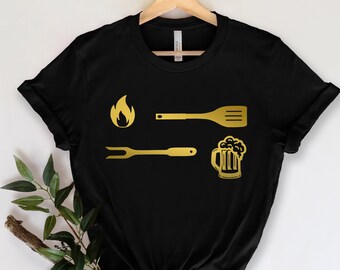 May include: Black t-shirt with a gold graphic of a flame, spatula, fork, and beer mug.