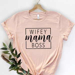 May include: A pale pink t-shirt with a black square graphic that says "WIFEY mama BOSS" in a cursive font.