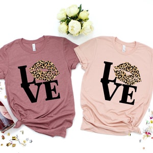 Pu&ograve; includere: Due magliette con la parola "LOVE" in lettere nere e un design a labbra con stampa leopardata. Le magliette sono color malva e rosa chiaro.