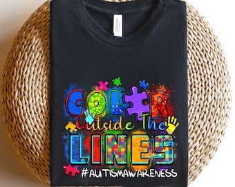 May include: Black t-shirt with a colorful graphic that says "Color Outside The Lines" and includes puzzle pieces. The graphic also includes the hashtag #autismawareness.