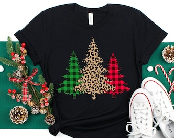 May include: Black t-shirt with a design of three Christmas trees. The trees are decorated with green plaid, leopard print, and red plaid.