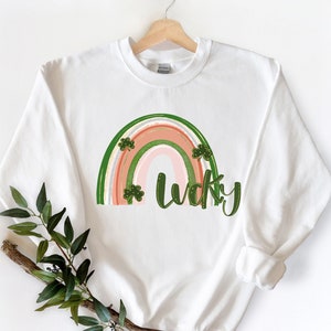 May include: White sweatshirt featuring a rainbow design with the word "lucky" in green lettering. The rainbow is decorated with green shamrocks.