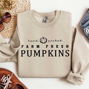 May include: A beige sweatshirt with the text "hand picked FARM FRESH PUMPKINS" in black lettering. A small black and white pumpkin graphic is above the text.