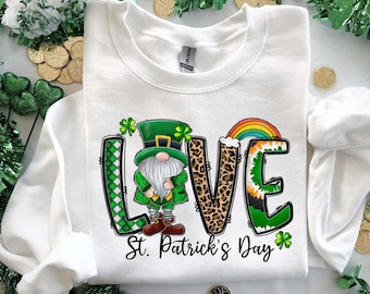 May include: White sweatshirt with a green, white, and black "LOVE" graphic featuring a leprechaun, rainbow, and shamrock. The text "St. Patrick's Day" is below the graphic.