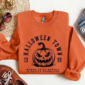 May include: Orange sweatshirt with a black graphic of a pumpkin with the text "Halloween Town 1998" and the phrase "Where being normal is vastly overrated".