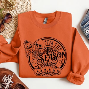 May include: Orange sweatshirt with a black graphic design of a skeleton holding a pumpkin and a tree with the text "Tis the Season".