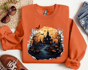 May include: Orange sweatshirt with a Halloween-themed graphic featuring a spooky house, bats, and pumpkins against a backdrop of a full moon.