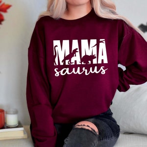 May include: A maroon sweatshirt with the text "MAMA saurus" in white. The text is surrounded by silhouettes of dinosaurs.