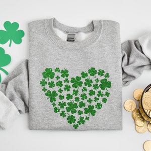 May include: A grey sweatshirt with a green glitter shamrock heart design. The shamrocks are arranged in a heart shape on the front of the sweatshirt.